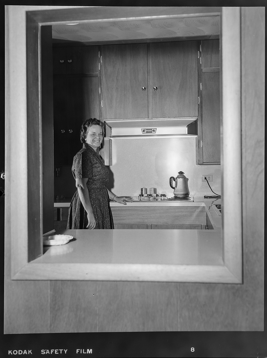 Black and white photo of woman standing in kitchen
