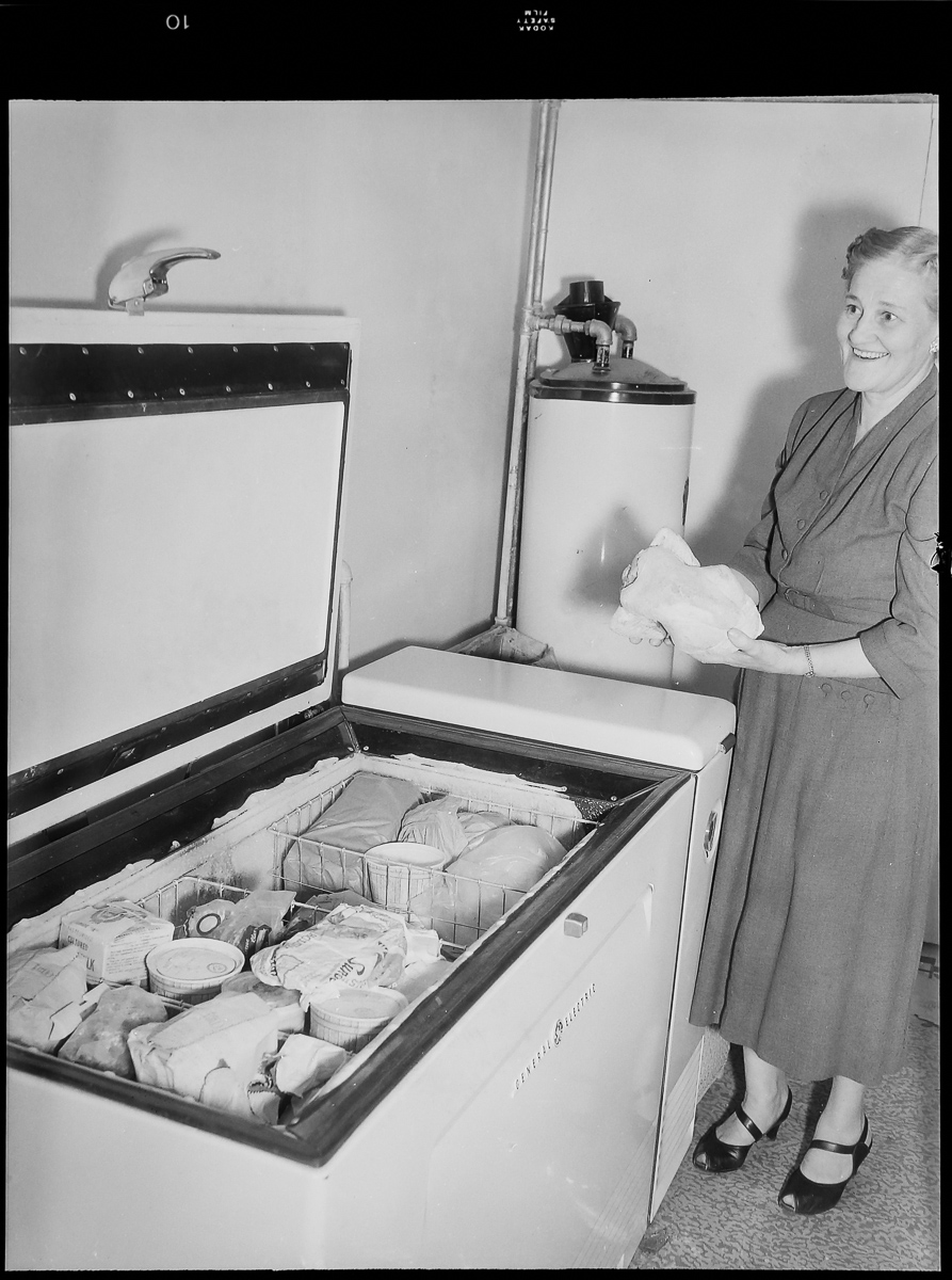 Black and white photo of woman standing in front of a chest freezer.